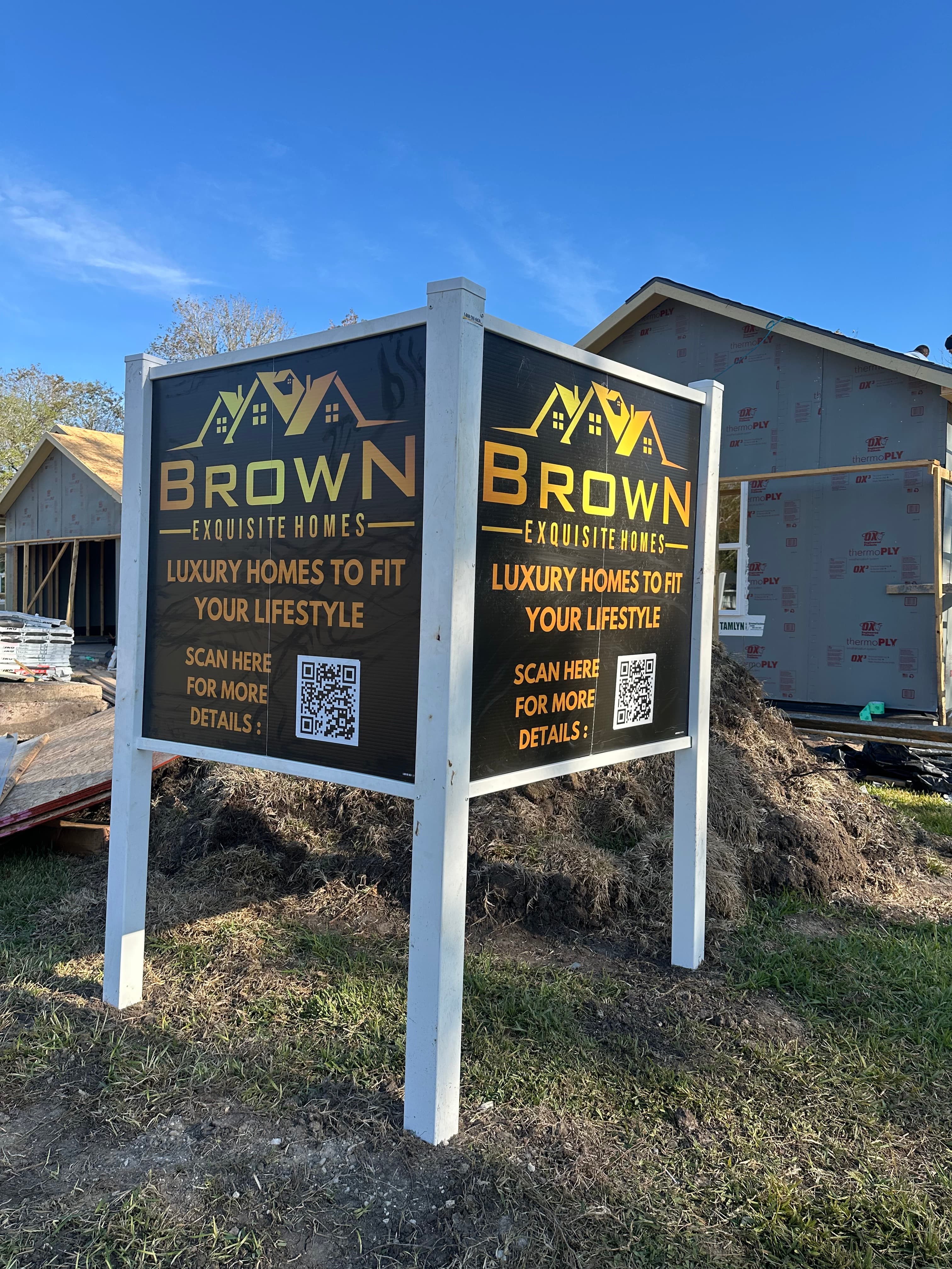 Brown Exquisite Homes sign on white posts in front of a house under construction.