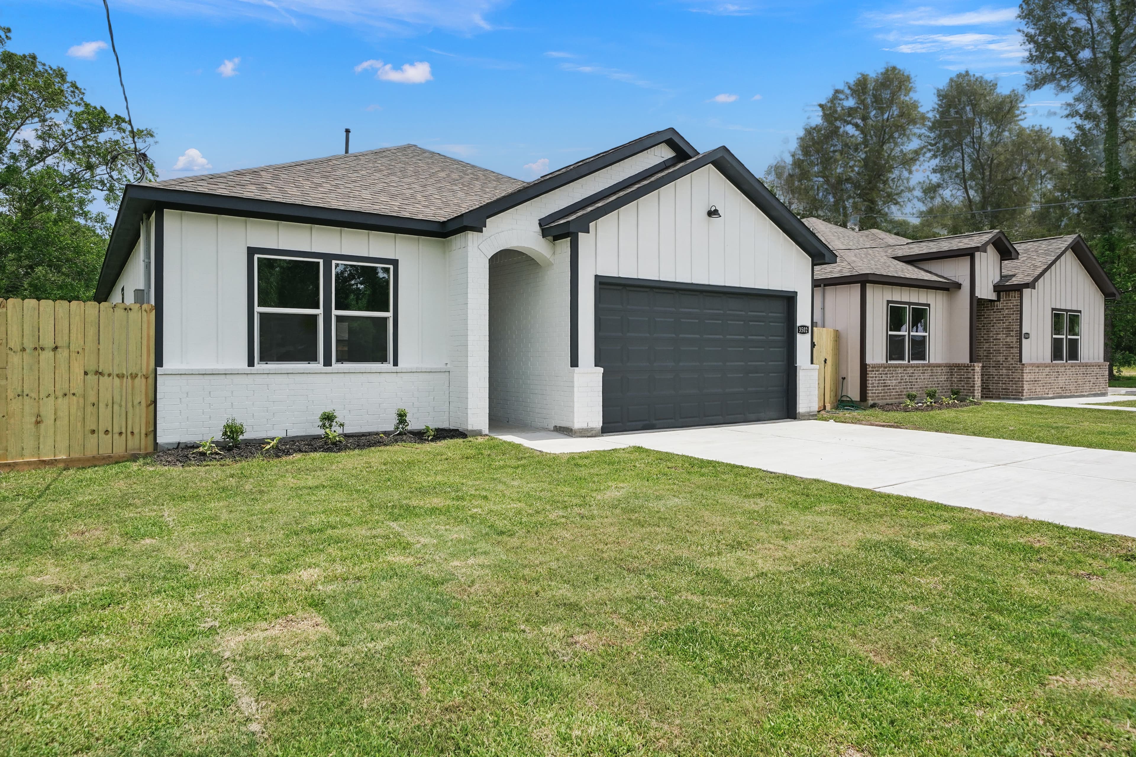 Modern white house with black trim, dark garage door, and a green front lawn.
